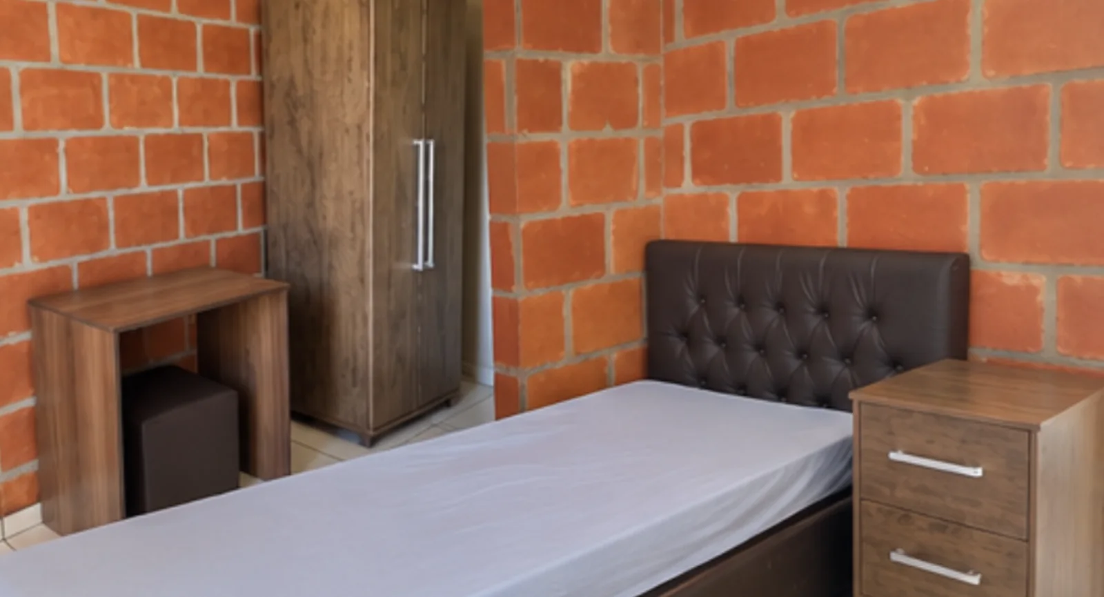 Quarto da pousada com uma cama de solteiro, armário e criado-mudo